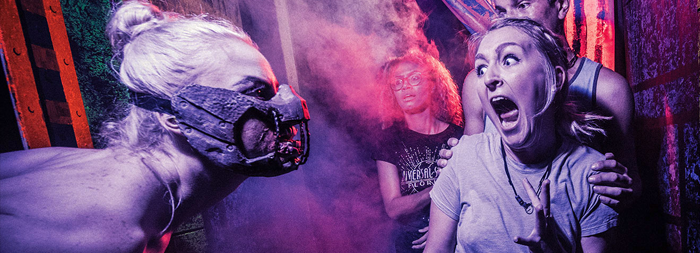 A group of people screaming while being chased by horror characters at Universal Orlando Resort’s Halloween Horror Nights.