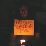 I Have Proof still: Larsen Deane as Alex holding a NO ONE BELIEVES ME sign by candlelight